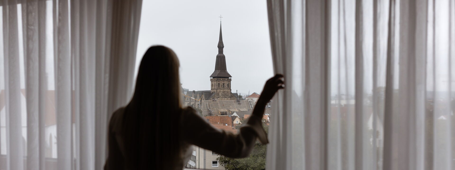 Frau schaut aus einem Fenster vom Remarque Hotel auf die Osnabrücker Innenstadt Frau schaut aus einem Fenster vom Remarque Hotel auf die Osnabrücker Innenstadt
