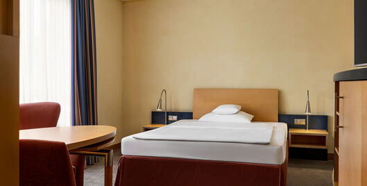 Standard Einzelzimmer mit Bett, zwei Nachtschränken, 2 Nachttischlampen, Fenster, Schreibtisch und Stuhl