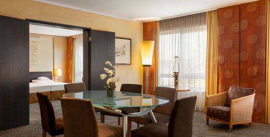 Hotel Remarque 2-Raum-Suite Wohnzimmer mit Tisch für 6 Personen, Stühlen, Wandbild, Stehlampe, Sessel