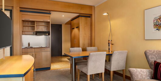 Junior Suite mit Tisch für 4 Personen, Sofa, Kitchenette, Schrank und Flur