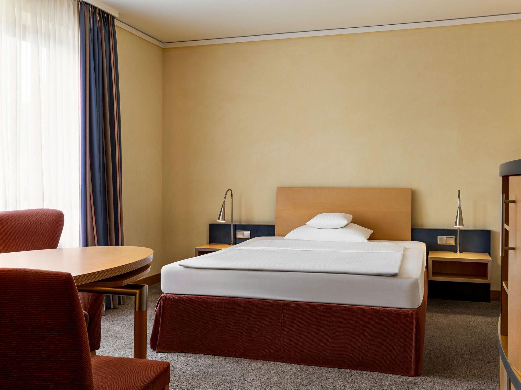 Standard Einzelzimmer mit Bett, zwei Nachtschränken, 2 Nachttischlampen, Fenster, Schreibtisch und Stuhl