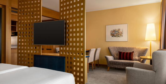 Junior Suite mit Doppelbett, Fernseher, Sofa, Sessel und Stehlampe