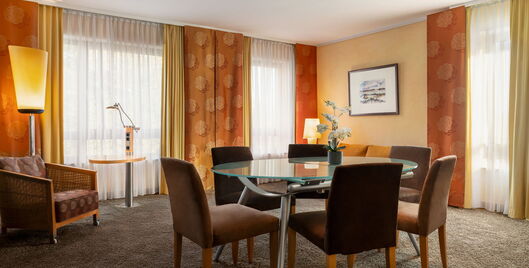 Hotel Remarque 2-Raum-Suite Wohnzimmer mit Tisch für 6 Personen, Stühlen, Wandbild, Stehlampe, Sessel