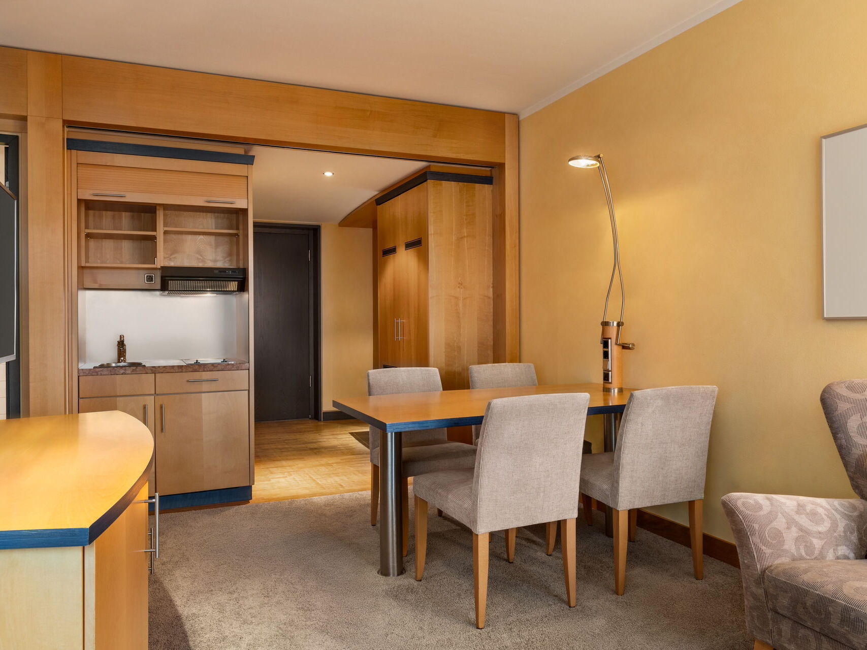 Junior Suite mit Tisch für 4 Personen, Sofa, Kitchenette, Schrank und Flur