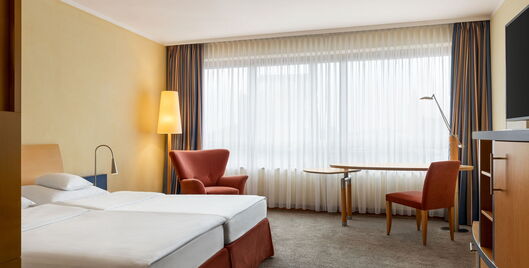 Doppelzimmer mit Doppelbett, Sessel, Fernseher, Tisch, Sessel, Stuhl und Fenster