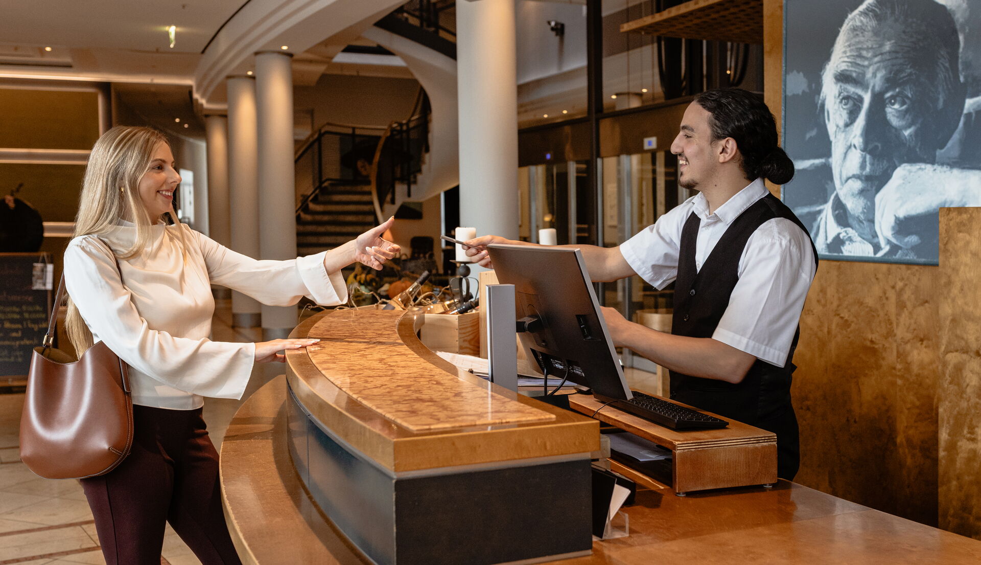 Ein Hotelgast nimmt mit einem Lächeln die Zimmerkarte vom Portier in der Hotellobby entgegen.